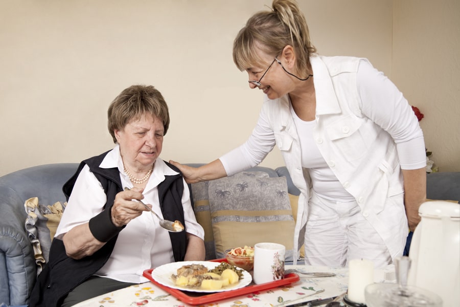 Frau vom Pflegedienst hilft älterer Frau beim Essen kochen