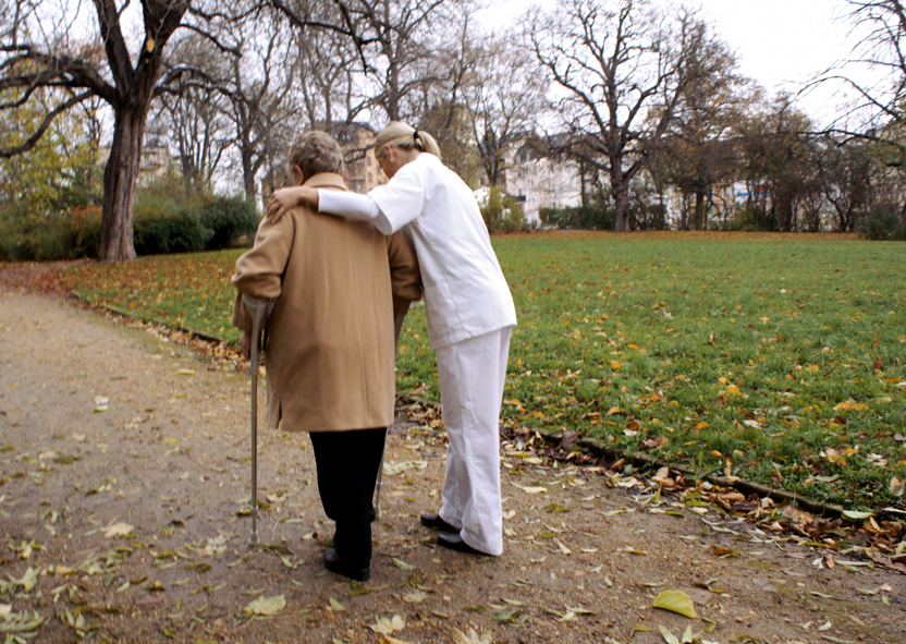 Frau vom Pflegedienst geht mit älterer Frau im Park spazieren